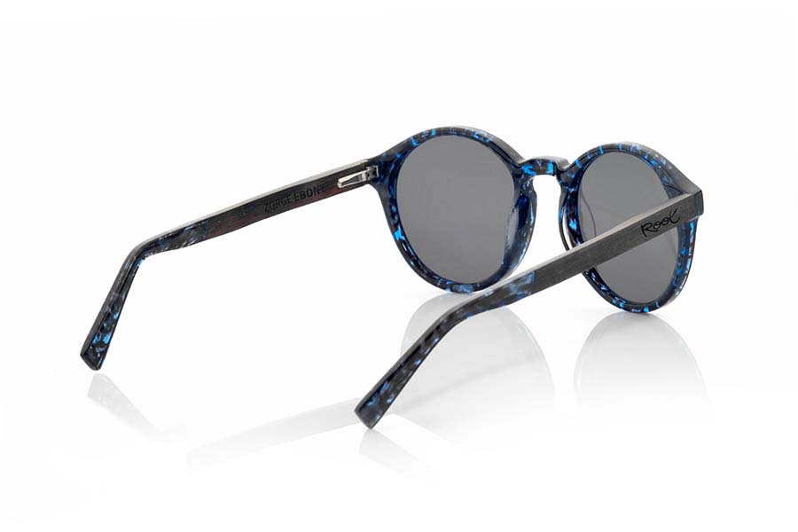 Gafas de Madera Natural de Ébano ZORGE. Las gafas de sol ZORGE de la serie MIXED PREMIUM están fabricadas con el frontal en acetato de calidad en color carey negro con destellos azules y las varillas en madera de EBANO natural terminadas en varilla cubiertas de acetato carey con destellos azules que permiten ser ajustadas en caso necesario. Se trata de un modelo redondeado de formas sugerentes que quedan perfectamente a personas de ambos sexos y han sido combinadas de serie con lentes grises o azul REVO. Te sorprenderá la calidad de los materiales y su terminación perfecta. Medida frontal: 140x51mm Venta al Por Mayor y Detalle | Root Sunglasses® 